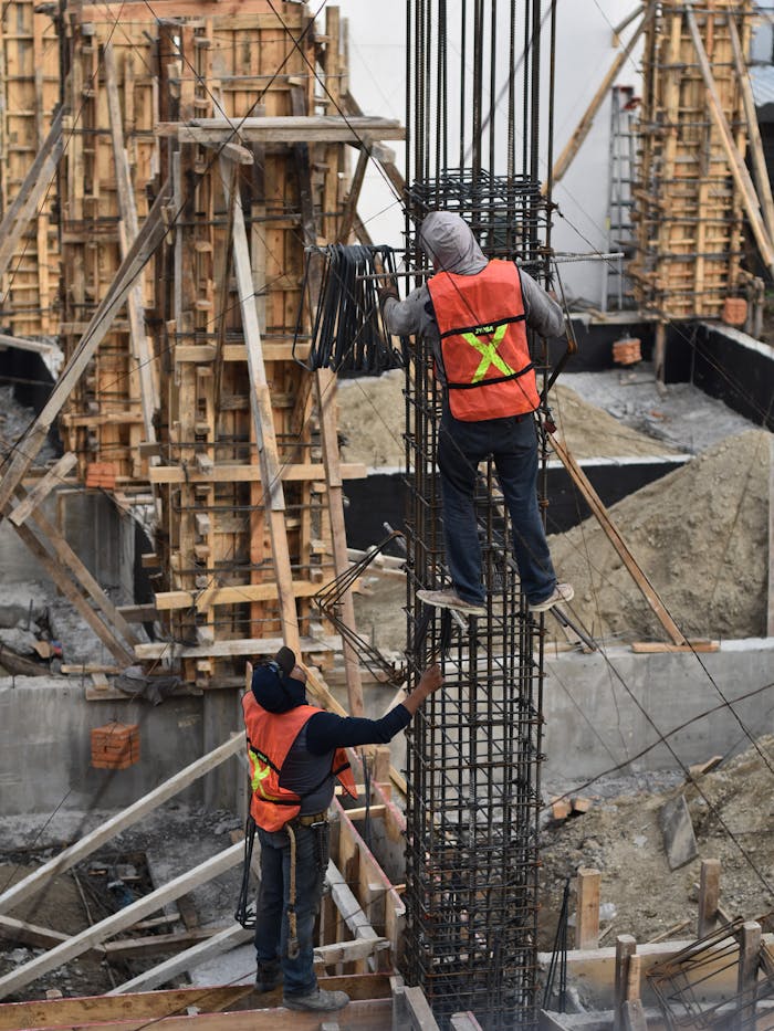 services-03 Two workers in safety vests climb a steel structure on a busy construction site.