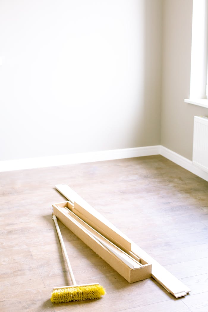 about-01 An empty room with wood planks and a broom, ready for renovation.