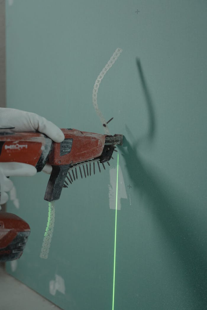 gallery-2 Close-up of a handyman using a laser level and nail gun for drywall installation.