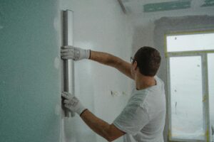 Services A man in a white shirt and gloves using a metal ruler for indoor wall renovation work.